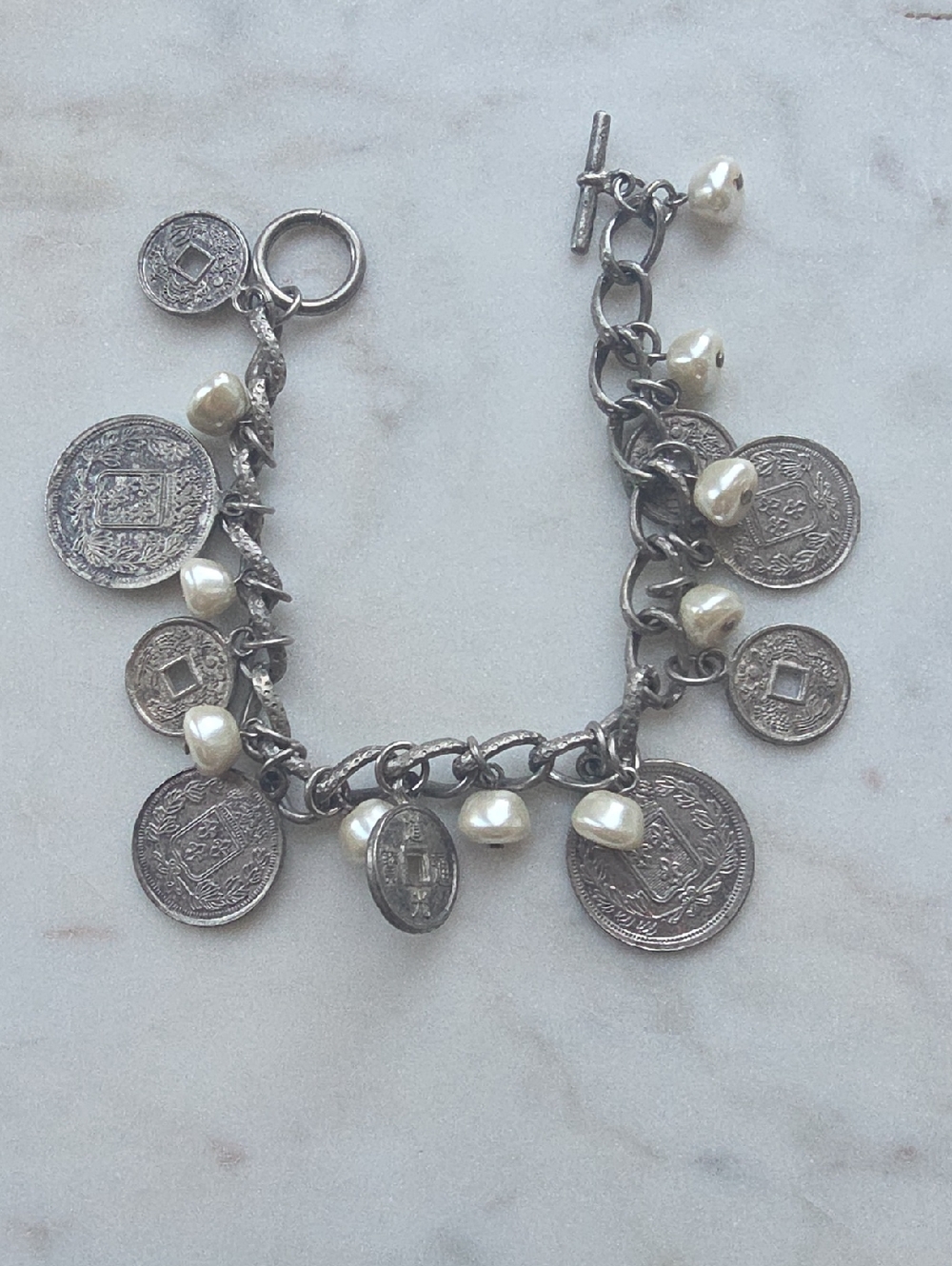Vintage-style charm bracelet features A Mix Of Coin Charms And Faux Pearls